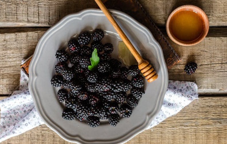 A plate of blackberries with honey pot next to it. 