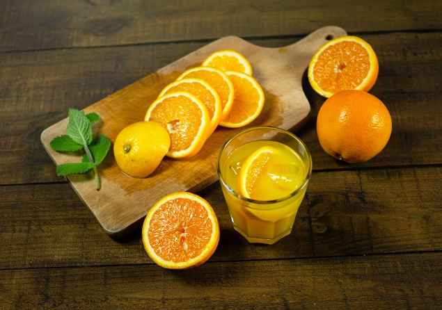 Oranges cut up on a wooden cutting board next to a glass of fresh orange juice.