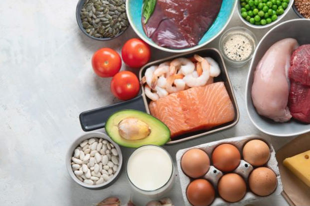 Healthy food on a kitchen counter like chicken, beef, salmon, shrimp, eggs, avocado, tomatoes, peas, nuts and milk.