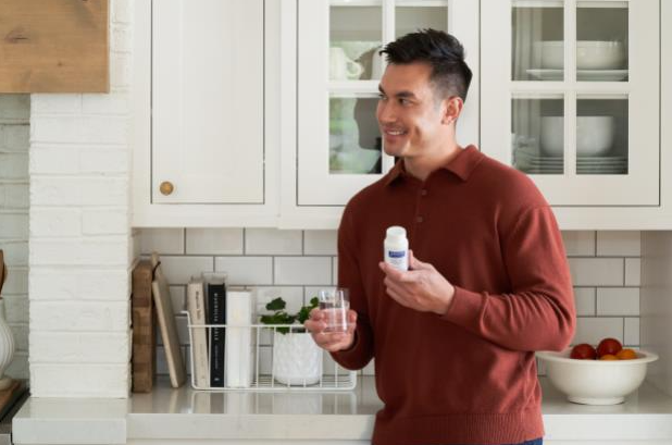 A man taking holding a glass of water and his Pure Encapsulations vitamins in the kitchen.