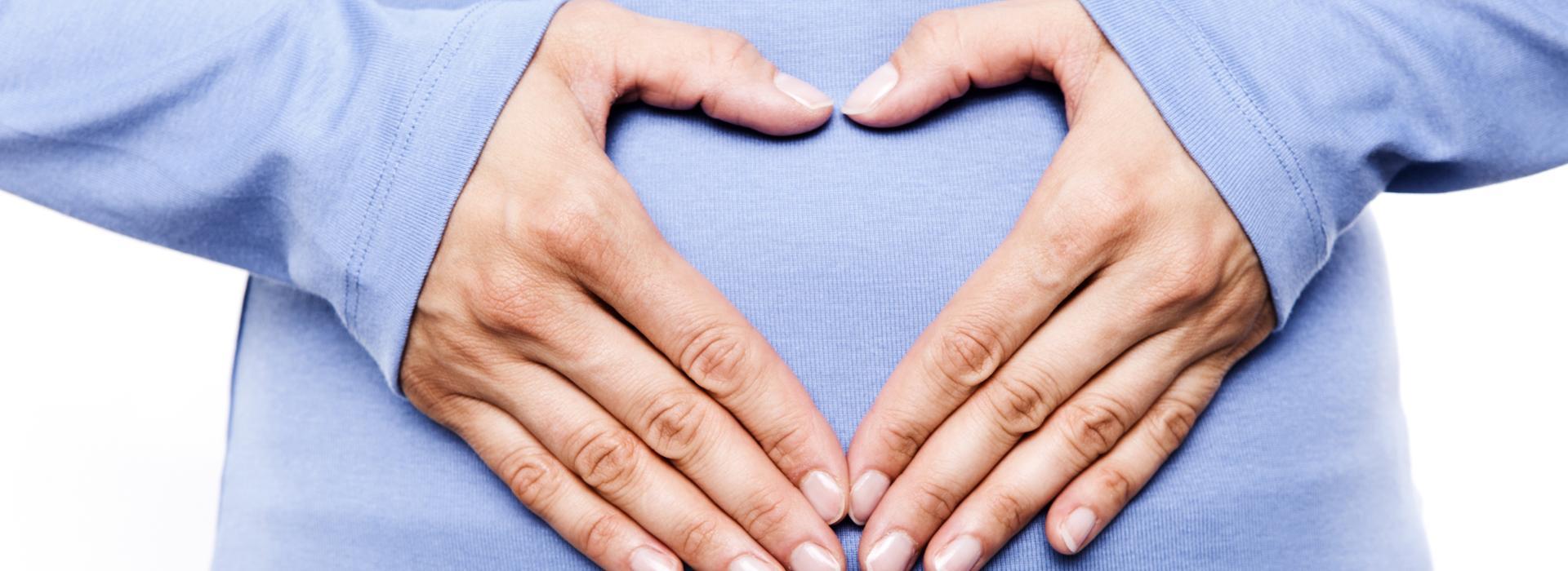 Women touching her stomach and making a heart shape with her hands