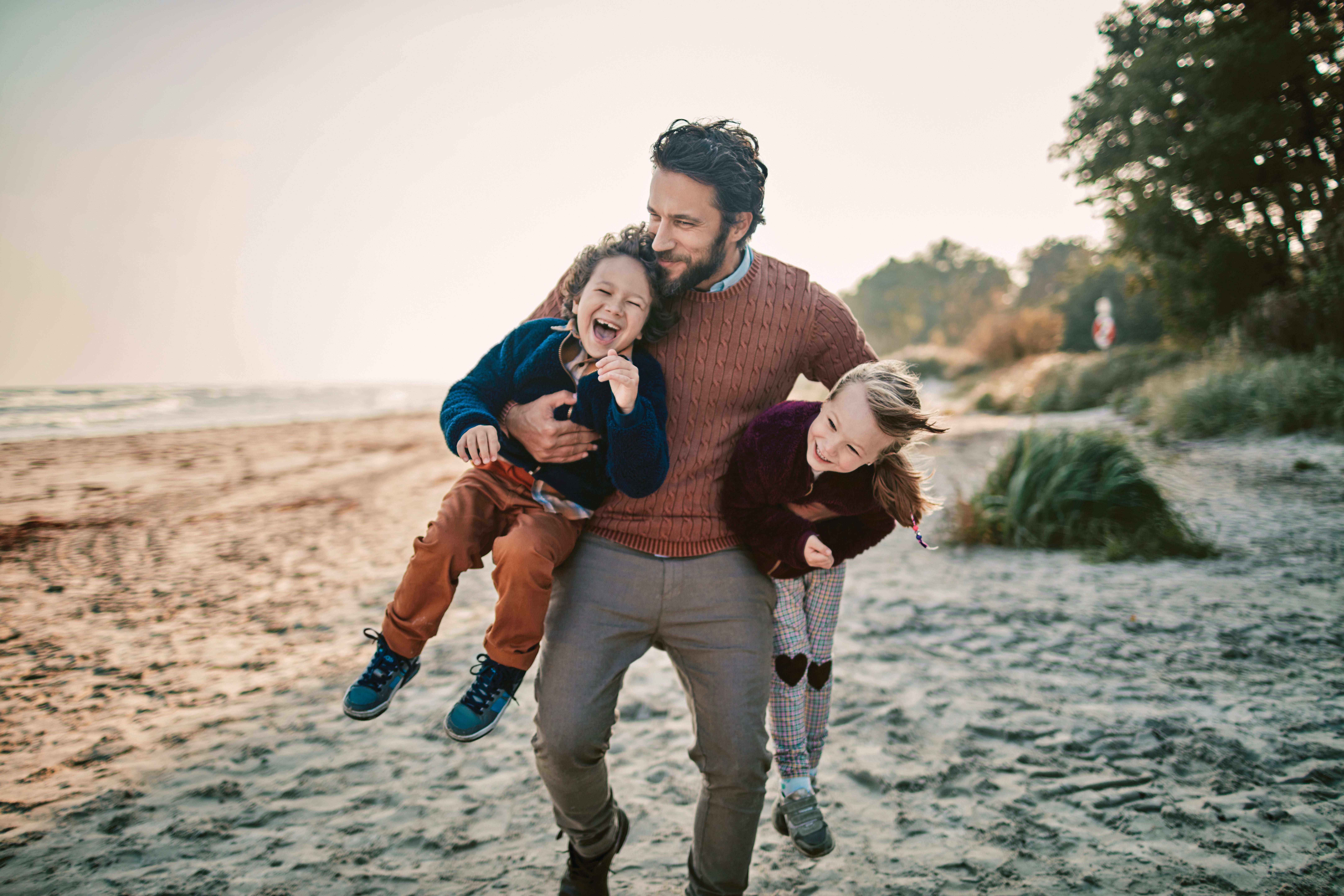 Dad at the beach with this two kids carrying them
