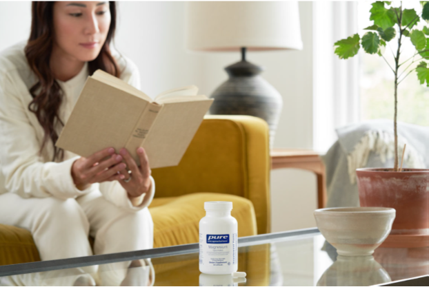 A women reading a book in her living room with a pure encapsulations supplement bottle on her coffee table