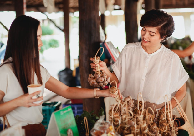 Two women shopping at a farmers market and picking out garlic.