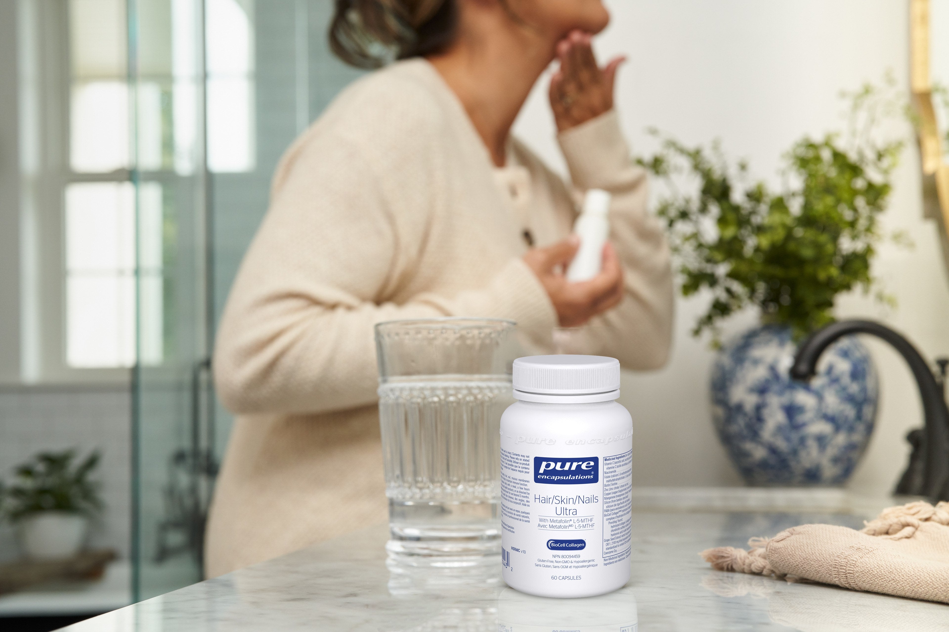 Pure Encapsulations product on a counter next a glass of a water and women getting ready for her day in the background.