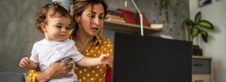 A women working on her laptop while holding her daughter