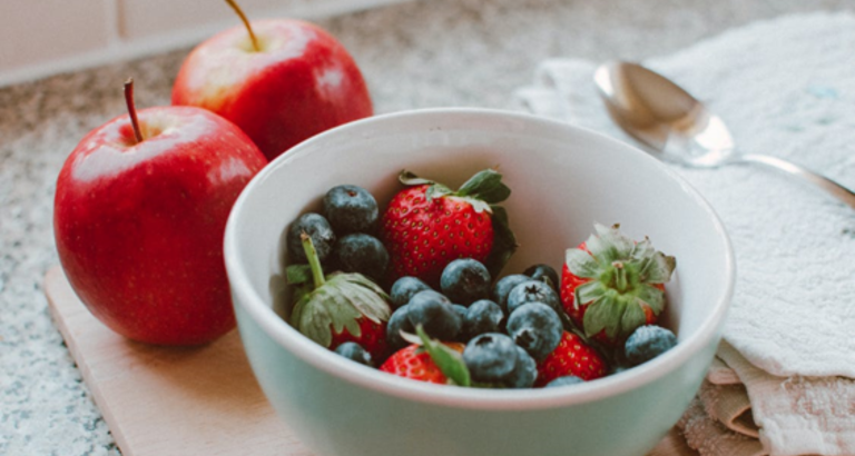 Strawberries and blueberries in a bowl with red apples next to it