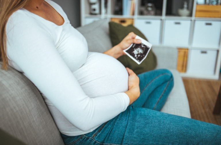 Pregnant women sitting on the couch and holding an image of her ultrasound.