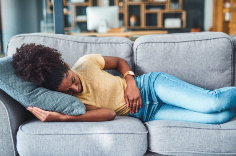 Women laying on the couch and holding her stomach due to stomach pain.