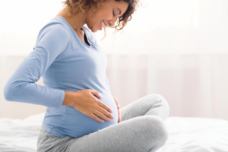 A women smiling and looking down at her pregnant stomach.