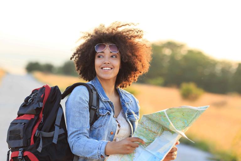 Une femme sac à dos à l’extérieur et souriant avec une carte.