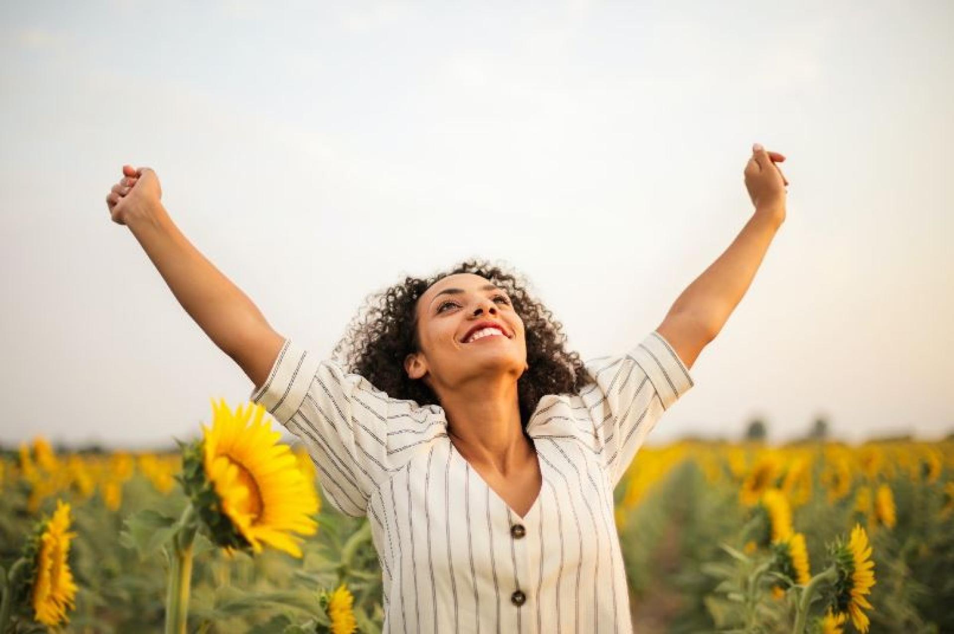 Women smiling and stretching her arms in a sunflower field