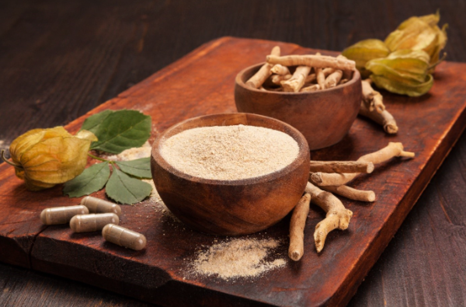 Aswagandha root and powder in a bowl with ashwaganda capsule supplements on a kitchen counter.