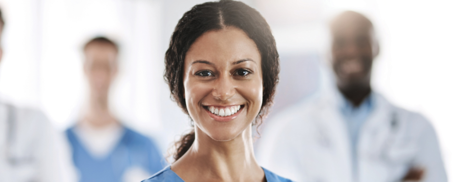 Women doctor crossing her arms and smiling with other medical professionals smiling in the background.  